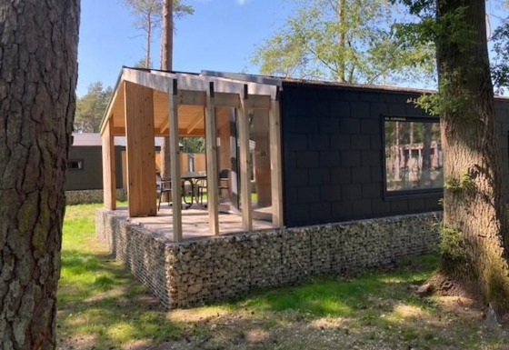Panorama Cottage, een tiny house met moderne glazen gevel en terras, omgeven door bomen en zonlicht.