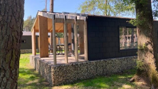 Panorama Cottage, ein Tiny House mit moderner Glasfassade und Terrasse im Grünen unter Bäumen.