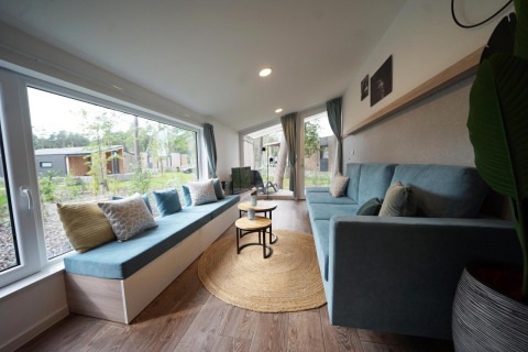 Lyst og hyggeligt opholdsområde i Panorama Cottage, et tiny house i Hoge Kempen, Belgien, med store vinduer.