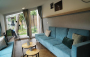 Moderne stue i et tiny house ved Hoge Kempen, Belgien, med blå sofaer, runde borde og store vinduer.