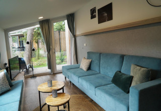 Moderne stue i et tiny house ved Hoge Kempen, Belgien, med blå sofaer, runde borde og store vinduer.