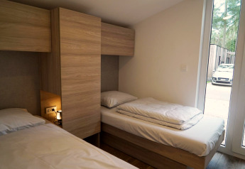 Slaapkamer met twee éénpersoonsbedden en houten meubels aan Panorama Cottage, Hoge Kempen, België, auto zichtbaar buiten.