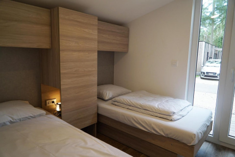 Slaapkamer met twee eenpersoonsbedden en houten kasten in Panorama Cottage, Hoge Kempen, België, met auto buiten.