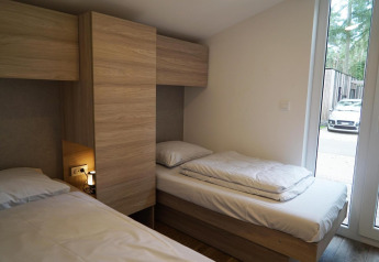 Dormitorio con dos camas individuales y armarios de madera en Panorama Cottage, Hoge Kempen, Bélgica, con coche afuera.
