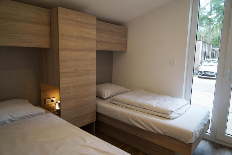 Dormitorio con dos camas individuales y armarios de madera en Panorama Cottage, Hoge Kempen, Bélgica, con coche afuera.