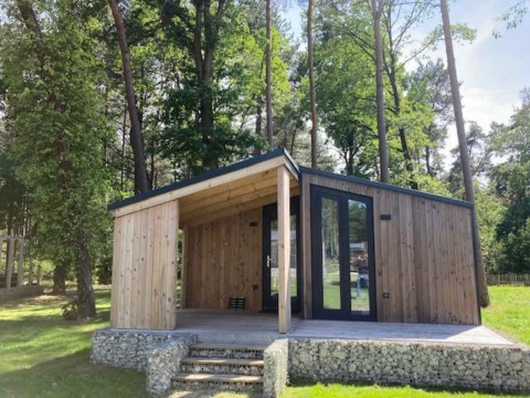 Panorama Cottage, une petite maison en bois à Hoge Kempen, Belgique, entourée d’arbres et de verdure.
