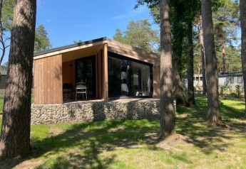 Moderna casa pequeña Panorama Cottage en Hoge Kempen, Bélgica, rodeada de altos árboles y vegetación natural.