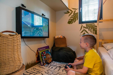 Boy playing video games in Kids Adventure cottage at Hoge Kempen, Belgium, cozy decorated room.