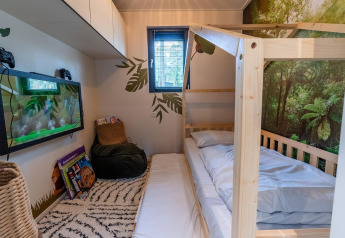 Chambre du Kids Adventure cottage à Hoge Kempen, Belgique, avec lit en bois et décor forêt tropicale.