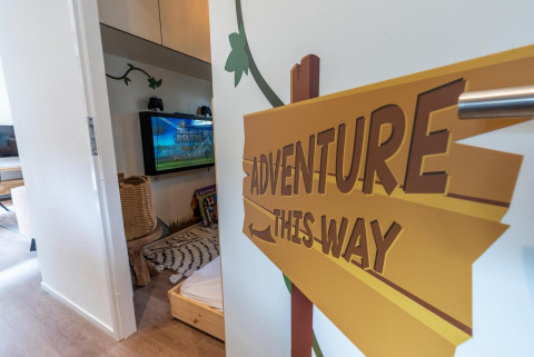 Stanza per bambini con cartello 'Adventure This Way' al Kids Adventure cottage, Hoge Kempen, Belgio.