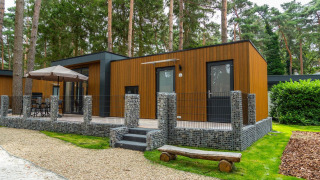 Moderna cabaña de madera en el bosque con terraza, muebles de exterior y pared de piedra.