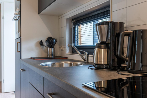 Cuisine moderne de lodge avec cafetière, bouilloire, ustensiles de cuisine et fenêtre à stores.