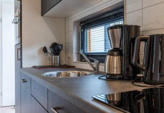 Cuisine moderne de lodge avec cafetière, bouilloire, ustensiles de cuisine et fenêtre à stores.