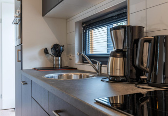 Moderne køkken i en lodge med kaffemaskine, elkedel, køkkenredskaber og vindue med persienner.