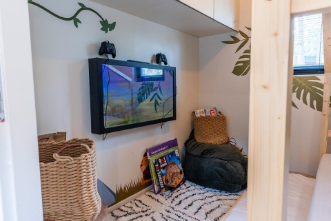 Rincón acogedor en Kids Adventure cottage con televisor, consolas, libros y asientos cómodos para niños.
