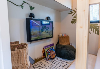 Coin confortable pour enfants au Kids Adventure cottage avec TV, manettes de jeu, livres et pouf moelleux.