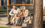En familie på fire sidder sammen på trappen foran Papendaal lodge i Hoge Kempen, Belgien, på en solrig dag.