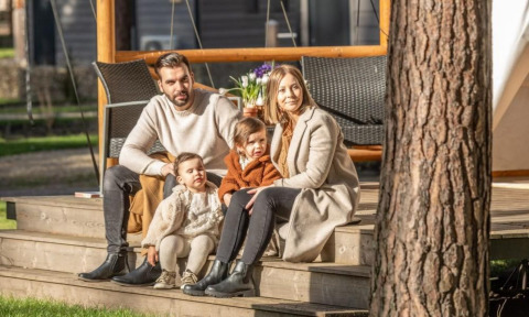 Une famille de quatre est assise ensemble sur les marches du Papendaal lodge à Hoge Kempen, Belgique, par temps ensoleillé.