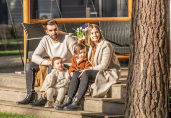 Una famiglia di quattro persone è seduta insieme sui gradini davanti al Papendaal lodge a Hoge Kempen, Belgio, in una giornata di sole.