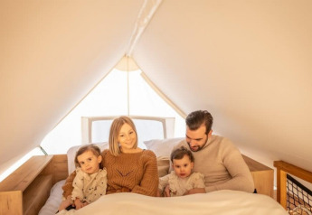 Een familie zit samen op het bed in de Papendaal lodge te Hoge Kempen, België, in sfeervol licht.