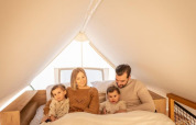Una famiglia seduta insieme su un letto al Papendaal lodge, Hoge Kempen, Belgio, circondata da luce calda.