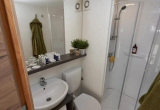 Badeværelse med vask, toilet, brusekabine og grønne håndklæder i Papendaal Lodge, Hoge Kempen, Belgien.