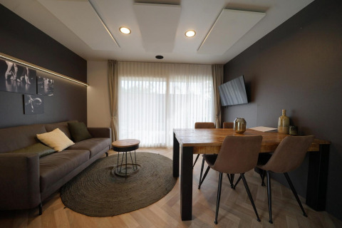 Sala de estar moderna en Lieteberg cottage, Hoge Kempen, Bélgica, con sofá, mesa, arte y cortinas claras.