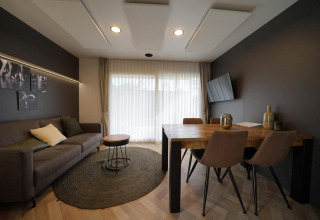 Sala de estar moderna en Lieteberg cottage, Hoge Kempen, Bélgica, con sofá, mesa, arte y cortinas claras.