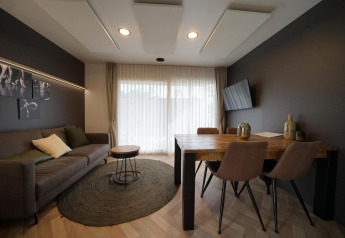 Sala de estar moderna en Lieteberg cottage, Hoge Kempen, Bélgica, con sofá, mesa, arte y cortinas claras.