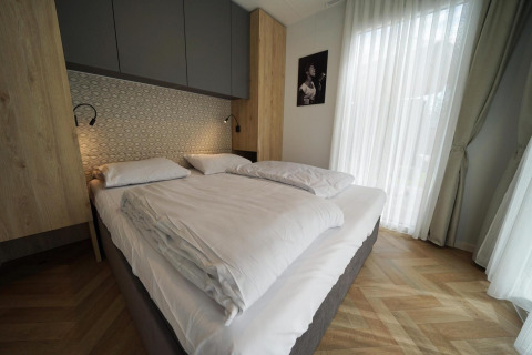 Dormitorio moderno con cama doble, detalles de madera y gran ventanal en la cabaña Lieteberg, Bélgica.