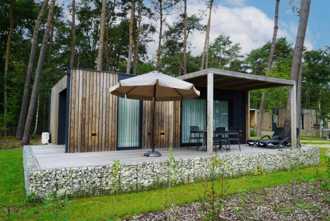 Trælodge ved Lieteberg cottage i Hoge Kempen, Belgien, omgivet af skov og med terrasse og møbler.