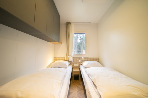 Dormitorio luminoso con dos camas individuales en la cabaña Lieteberg, Hoge Kempen, Bélgica, decorado simple.