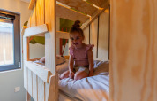 Niña pequeña sentada en la cama en una cabaña infantil en Hoge Kempen, Bélgica, con decoración de madera.