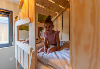 Niña pequeña sentada en la cama en una cabaña infantil en Hoge Kempen, Bélgica, con decoración de madera.