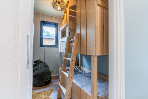 Camera per bambini con letti a castello in legno, pouf e finestra presso Kids cottage a Hoge Kempen, Belgio.