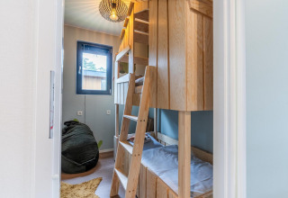 Camera per bambini con letti a castello in legno, pouf e finestra presso Kids cottage a Hoge Kempen, Belgio.