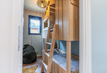 Habitación infantil con literas de madera, puf y ventana en Kids cottage de Hoge Kempen, Bélgica.