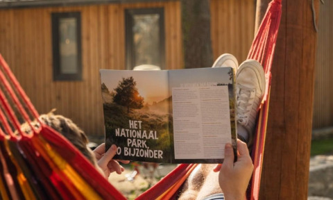Eine Person entspannt in einer Hängematte und liest eine Zeitschrift vor der Papendaal Lodge in Hoge Kempen, Belgien.