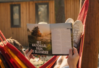 Eine Person entspannt in einer Hängematte und liest eine Zeitschrift vor der Papendaal Lodge in Hoge Kempen, Belgien.