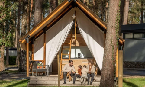 Een familie zit gezellig voor hun Papendaal lodge safaritent, midden in een bosrijke omgeving.