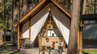 Een familie zit gezellig voor hun Papendaal lodge safaritent, midden in een bosrijke omgeving.