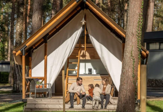 Een familie zit gezellig voor hun Papendaal lodge safaritent, midden in een bosrijke omgeving.