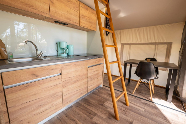 Cocina pequeña, mesa de comedor y escalera de madera en tienda safari Papendaal lodge en Hoge Kempen, Bélgica.