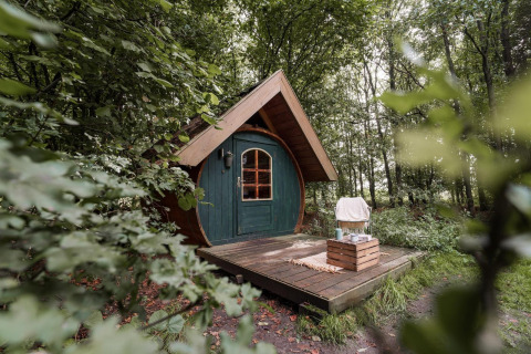 Kleines Holzhäuschen mit grüner Tür auf einer Holzterrasse im Wald bei RØSTIG Dorst, Niederlande.