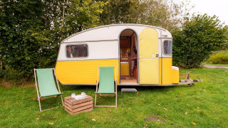 Caravan gialla e bianca con due sedie verdi al RØSTIG Dorst nei Paesi Bassi su prato verde.