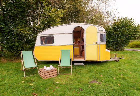 Gele en witte caravan met twee groene stoelen bij RØSTIG Dorst lodge in Nederland op gras.
