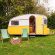 Gul og hvid retro campingvogn med to grønne stole ved RØSTIG Dorst i Holland på en græsplæne.