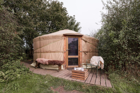 Yurt bij RØSTIG Dorst in Nederland, omgeven door bomen, met bank en stoelen op het houten terras.