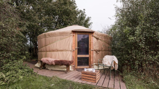 Yurt bij RØSTIG Dorst in Nederland, met houten terras, bank en stoelen, midden in de natuur.