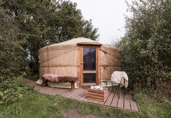 Yurt bij RØSTIG Dorst in Nederland, met houten terras, bank en stoelen, midden in de natuur.